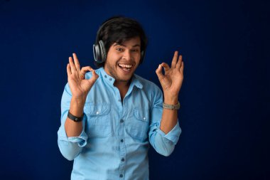 Portrait of a handsome young man enjoying music on headphones on blue background.