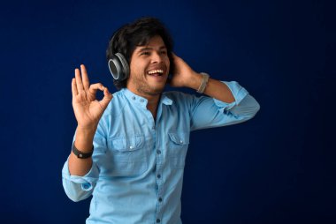 Portrait of a handsome young man enjoying music on headphones on blue background.