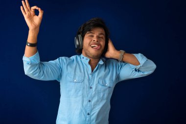 Portrait of a handsome young man enjoying music on headphones on blue background.