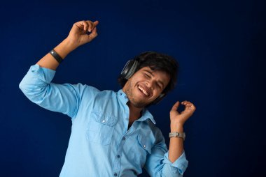 Portrait of a handsome young man enjoying music on headphones on blue background.