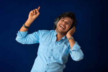 Portrait of a handsome young man enjoying music on headphones on blue background.