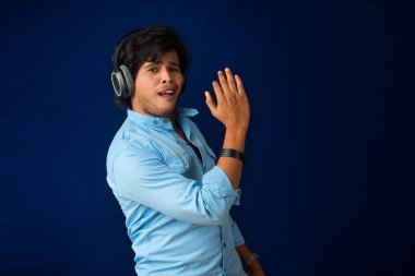 Portrait of a handsome young man enjoying music on headphones on blue background.