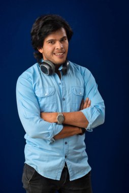 Portrait of a handsome young man enjoying music on headphones on blue background.