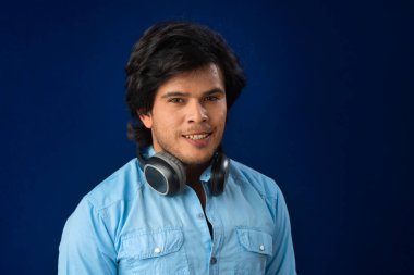 Portrait of a handsome young man enjoying music on headphones on blue background.