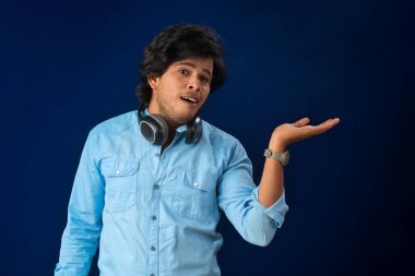 Portrait of a handsome young man enjoying music on headphones on blue background.