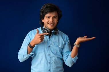 Portrait of a handsome young man enjoying music on headphones on blue background.