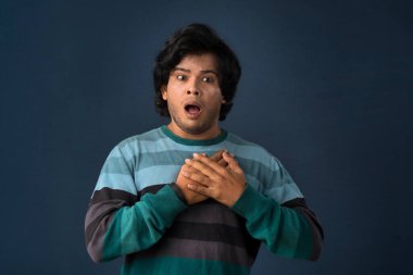 Unhappy young man having a heart attack or heartache over gray background. People, healthcare and health problem concept.