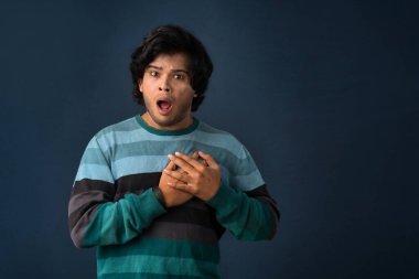 Unhappy young man having a heart attack or heartache over gray background. People, healthcare and health problem concept.