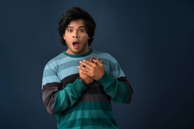 Unhappy young man having a heart attack or heartache over gray background. People, healthcare and health problem concept.