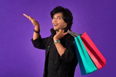 Beautiful Indian young handsome man holding and posing with shopping bags on a purple background