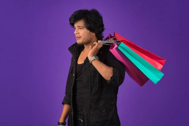 Beautiful Indian young handsome man holding and posing with shopping bags on a purple background