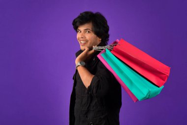 Beautiful Indian young handsome man holding and posing with shopping bags on a purple background