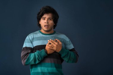 Unhappy young man having a heart attack or heartache over gray background. People, healthcare and health problem concept.