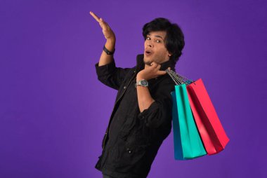 Beautiful Indian young handsome man holding and posing with shopping bags on a purple background