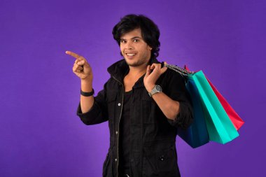 Beautiful Indian young handsome man holding and posing with shopping bags on a purple background