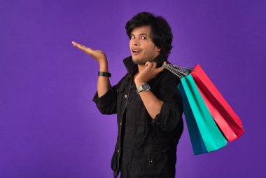 Beautiful Indian young handsome man holding and posing with shopping bags on a purple background