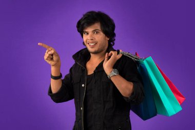 Beautiful Indian young handsome man holding and posing with shopping bags on a purple background