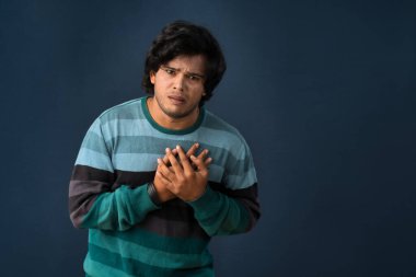 Unhappy young man having a heart attack or heartache over gray background. People, healthcare and health problem concept.
