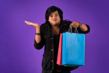 Beautiful Indian young handsome man holding and posing with shopping bags on a purple background