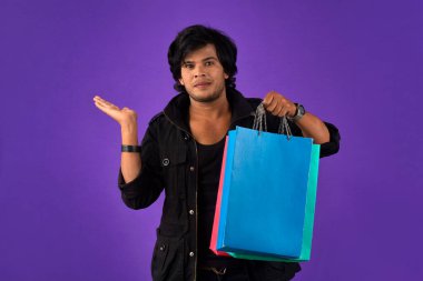 Beautiful Indian young handsome man holding and posing with shopping bags on a purple background
