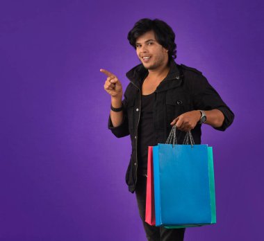 Beautiful Indian young handsome man holding and posing with shopping bags on a purple background