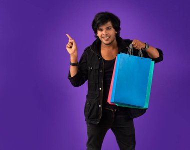 Beautiful Indian young handsome man holding and posing with shopping bags on a purple background