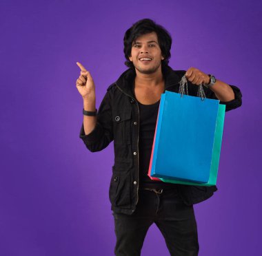 Beautiful Indian young handsome man holding and posing with shopping bags on a purple background