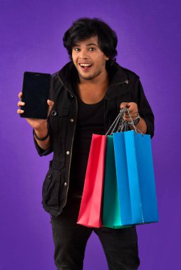 Portrait of a young man with a mobile phone or tablet smartphone and shopping bags in his hands.