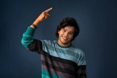 Portrait of a successful cheerful young man pointing and presenting something with hand or finger with a happy smiling face.