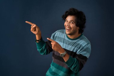 Portrait of a successful cheerful young man pointing and presenting something with hand or finger with a happy smiling face.