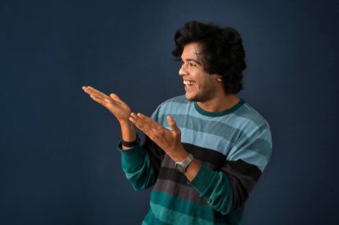 Portrait of a successful cheerful young man pointing and presenting something with hand or finger with a happy smiling face.