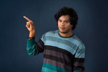 Portrait of a successful cheerful young man pointing and presenting something with hand or finger with a happy smiling face.