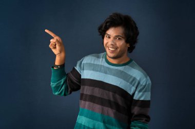 Portrait of a successful cheerful young man pointing and presenting something with hand or finger with a happy smiling face.
