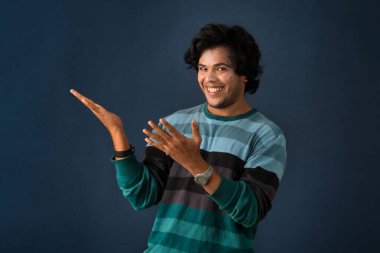 Portrait of a successful cheerful young man pointing and presenting something with hand or finger with a happy smiling face.