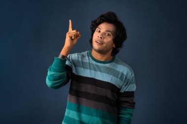 Portrait of a successful cheerful young man pointing and presenting something with hand or finger with a happy smiling face.