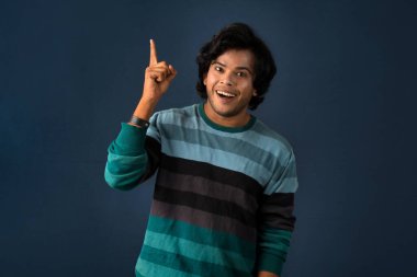 Portrait of a successful cheerful young man pointing and presenting something with hand or finger with a happy smiling face.