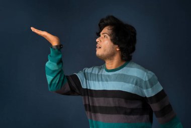 Portrait of a successful cheerful young man holding and presenting something on hand with a happy smiling face.