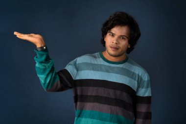 Portrait of a successful cheerful young man holding and presenting something on hand with a happy smiling face.