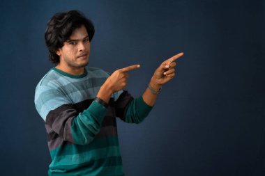 Portrait of a successful cheerful young man pointing and presenting something with hand or finger with a happy smiling face.