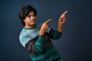 Portrait of a successful cheerful young man pointing and presenting something with hand or finger with a happy smiling face.
