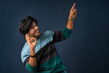 Portrait of a successful cheerful young man pointing and presenting something with hand or finger with a happy smiling face.