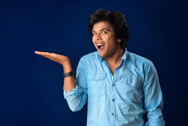 Portrait of a successful cheerful young man holding and presenting something on hand with a happy smiling face.
