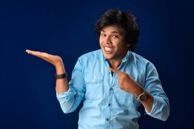 Portrait of a successful cheerful young man holding and presenting something on hand with a happy smiling face.