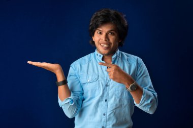 Portrait of a successful cheerful young man holding and presenting something on hand with a happy smiling face.
