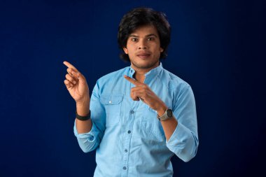 Portrait of a successful cheerful young man pointing and presenting something with hand or finger with a happy smiling face.