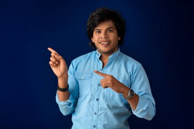 Portrait of a successful cheerful young man pointing and presenting something with hand or finger with a happy smiling face.