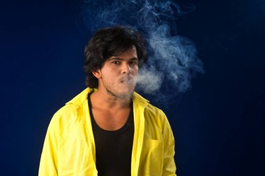 A young man smoking a cigarette and making a lot of smoke around.