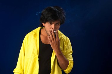 A young man smoking a cigarette and making a lot of smoke around.