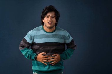 Unhappy man suffering from stomach ache over gray background. People, healthcare, and health problem concept.