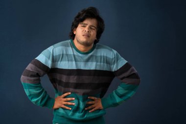 Unhappy man suffering from stomach ache over gray background. People, healthcare, and health problem concept.